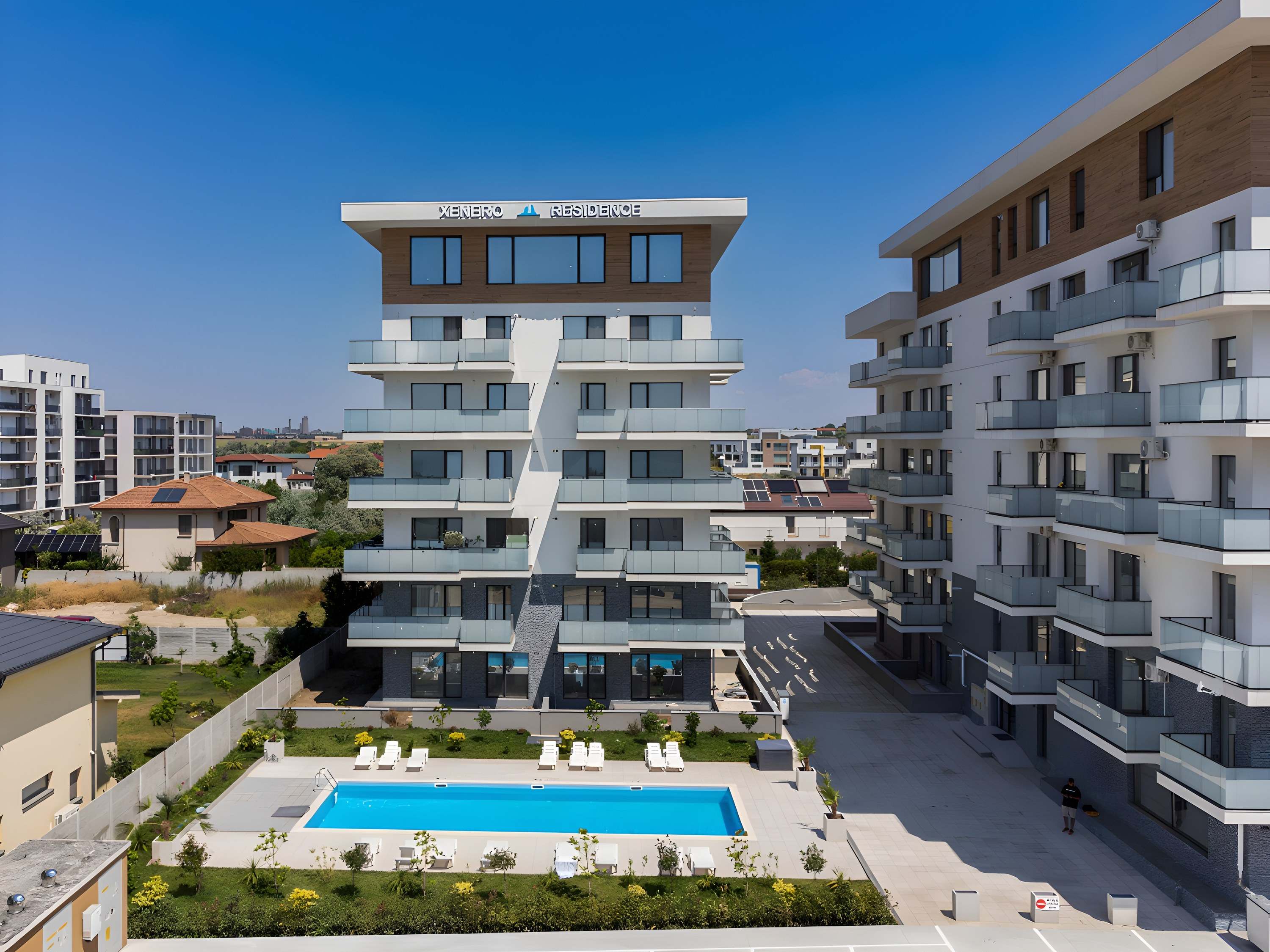 Curtea ansamblului XENERO Residence, cu piscina și șezlonguri albe între cele două clădiri