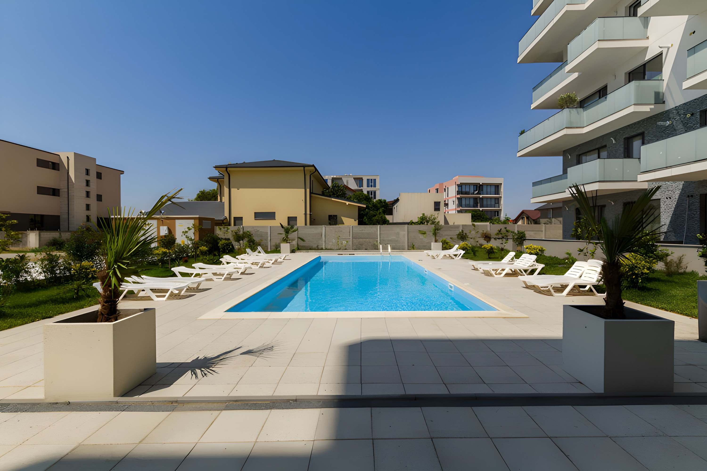 Piscina ansamblului, cu șezlonguri albe, lângă clădirea XENERO Residence