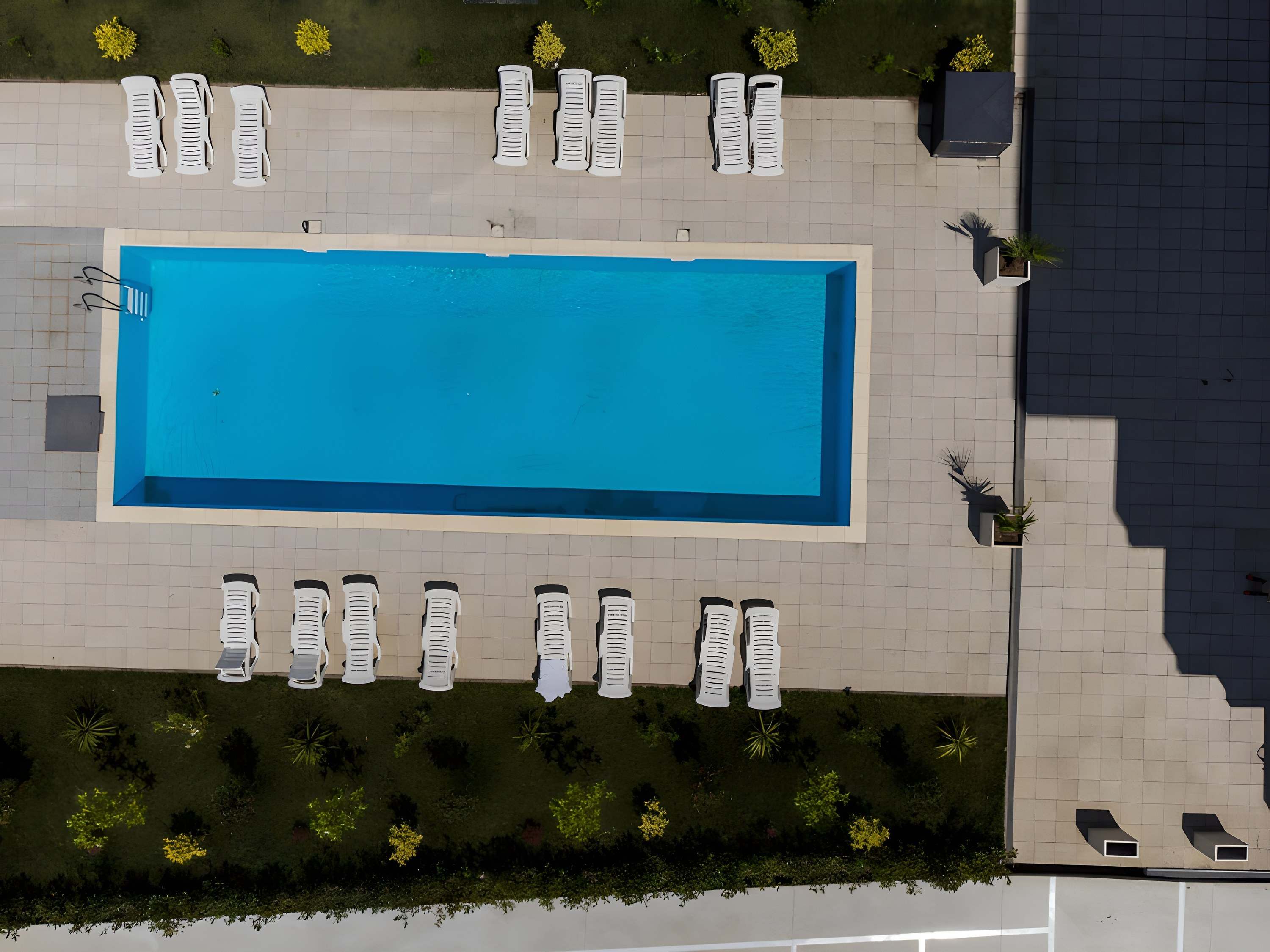 Piscina ansamblului văzută de sus, înconjurată de șezlonguri albe